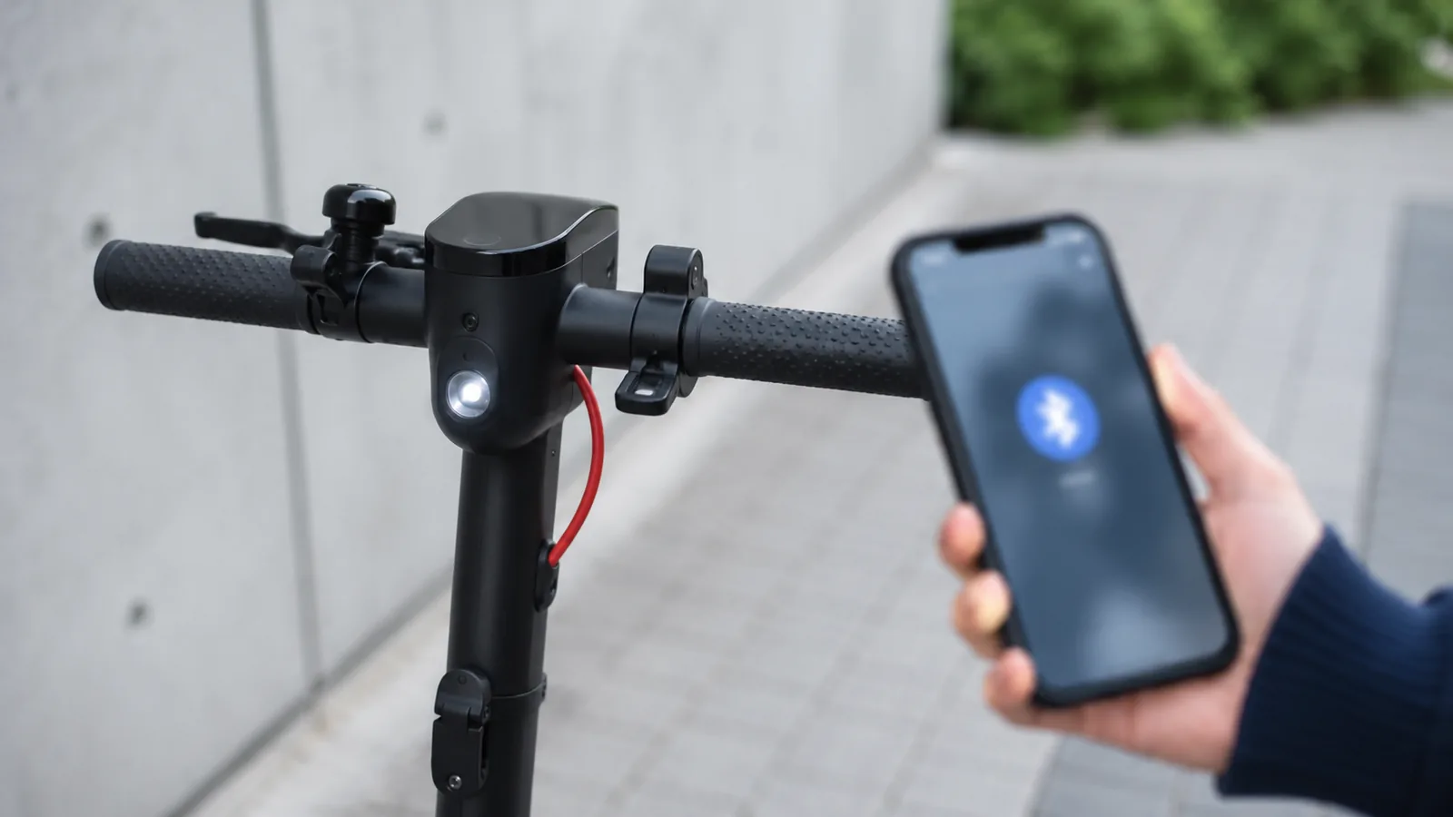 Nahaufnahme eines E-Scooter-Lenkers, daneben ein Smartphone mit Bluetooth-Symbol