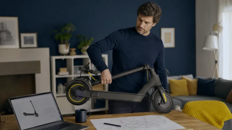Mann prüft im Wohnzimmer einen gefalteten E-Scooter neben einem Laptop