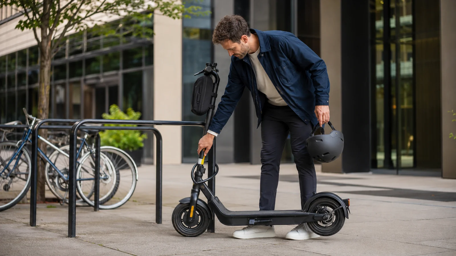 Mann schließt seinen E-Scooter an einem Fahrradständer an und hält einen Helm