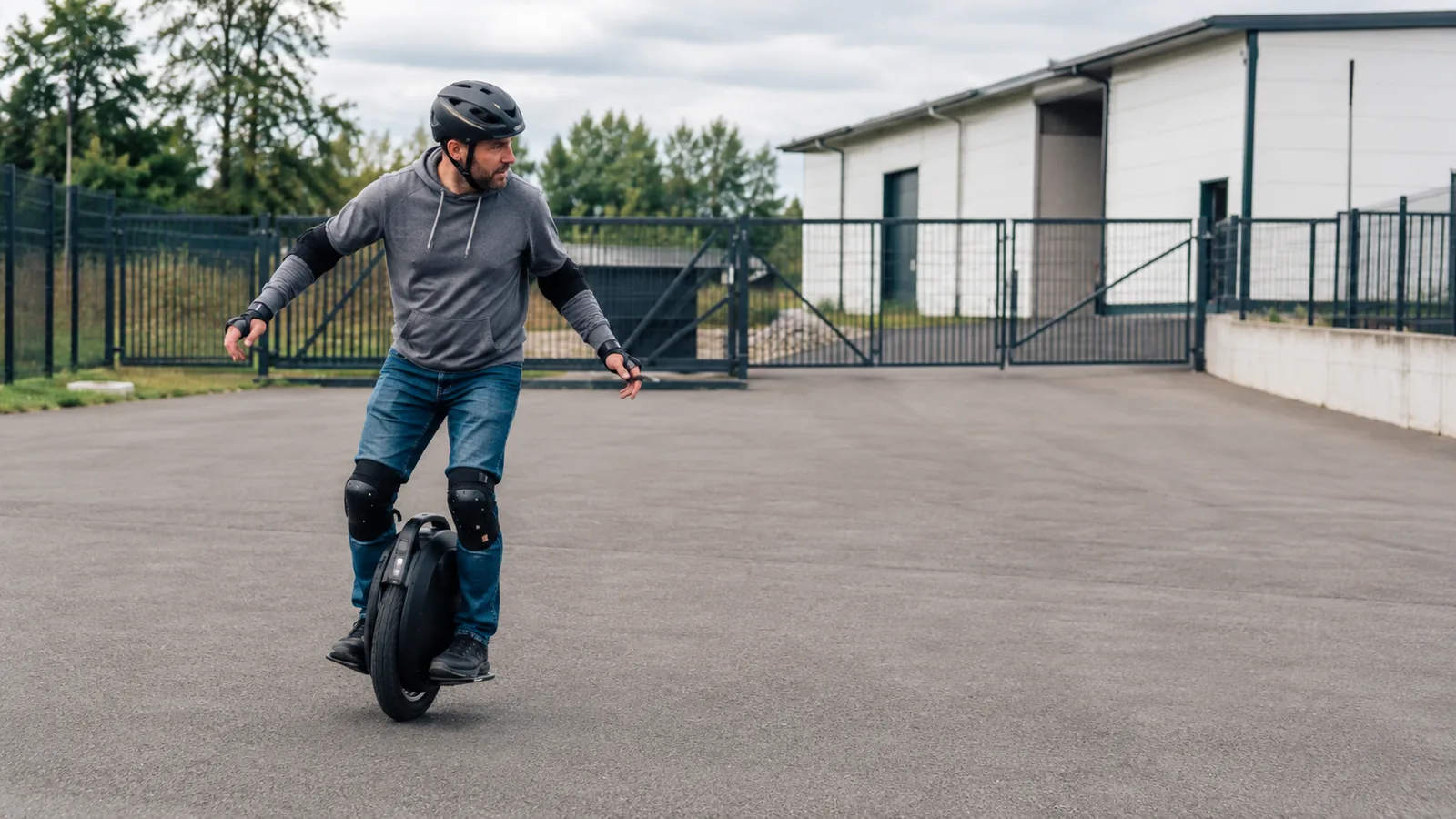 Erwachsener mit Helm und Protektoren faehrt E-Unicycle auf einer abgesperrten privaten Trainingsflaeche