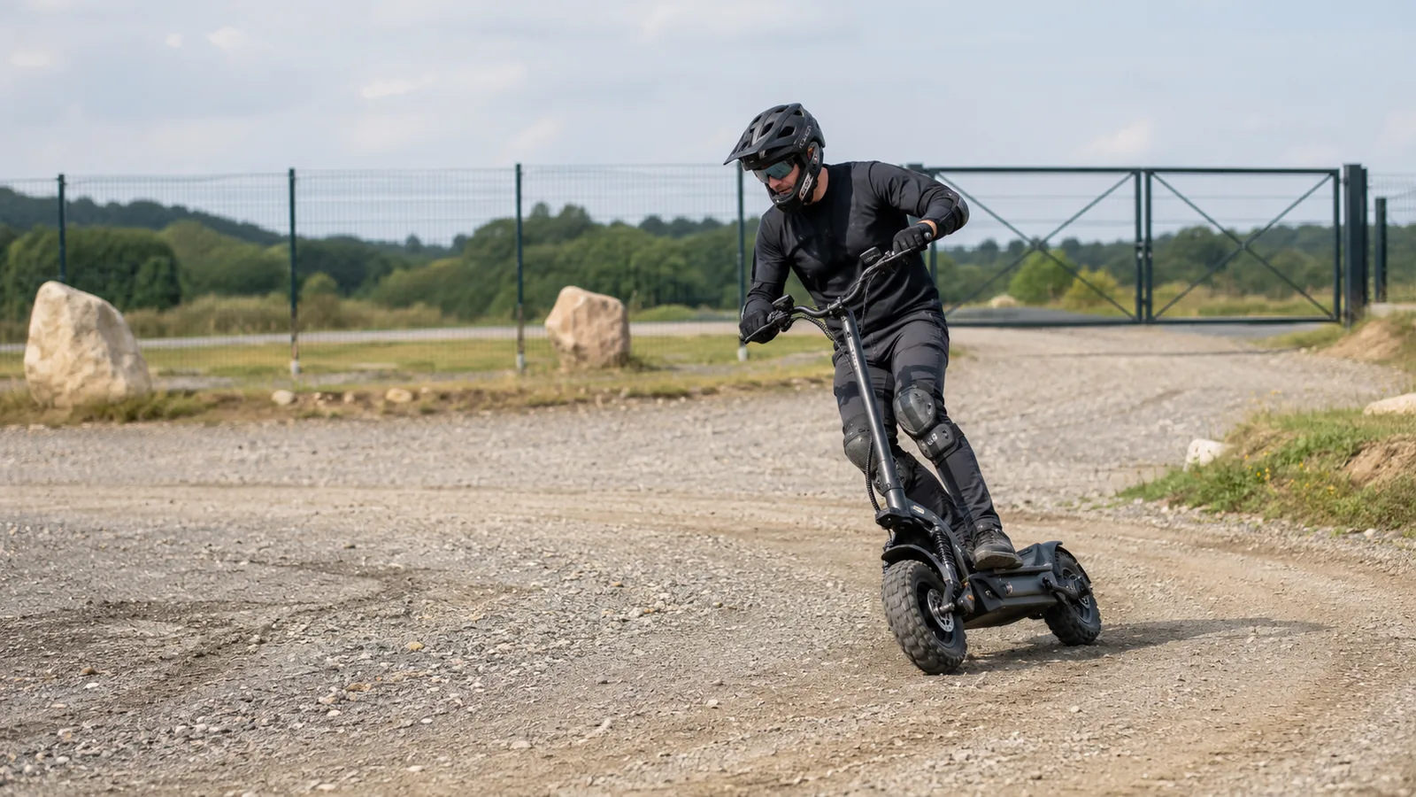 Person mit voller Schutzausrüstung fährt einen Offroad-E-Scooter mit groben Reifen auf einer abgesperrten privaten Schotter-Testfläche